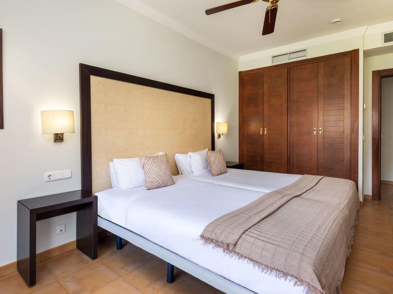 Pokój hotelowy z podwójnym łóżkiem, drewnianymi meblami i prostą dekoracją.