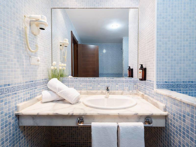 Łazienka hotelowa z marmurową umywalką, lustrem, ręcznikami i niebieskimi płytkami.