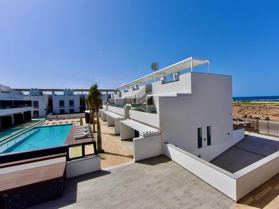 Complexe hôtelier blanc moderne avec piscine et vue sur la mer sous un ciel bleu clair.