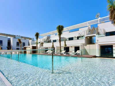 Moderner Außenpool mit klarem Wasser, weißen Gebäuden und Palmen unter blauem Himmel.