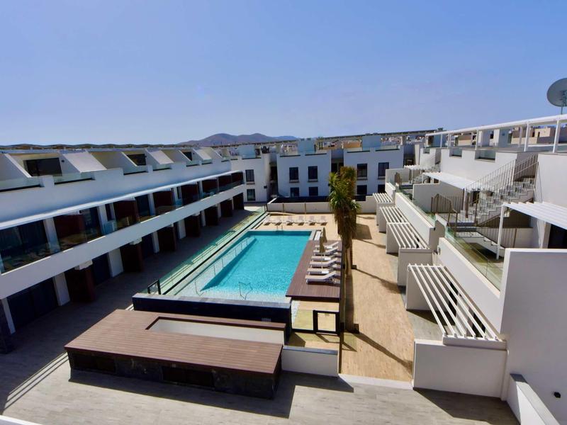Complexe hôtelier moderne avec piscine rectangulaire et bâtiment blanc de deux étages sous un ciel clair.