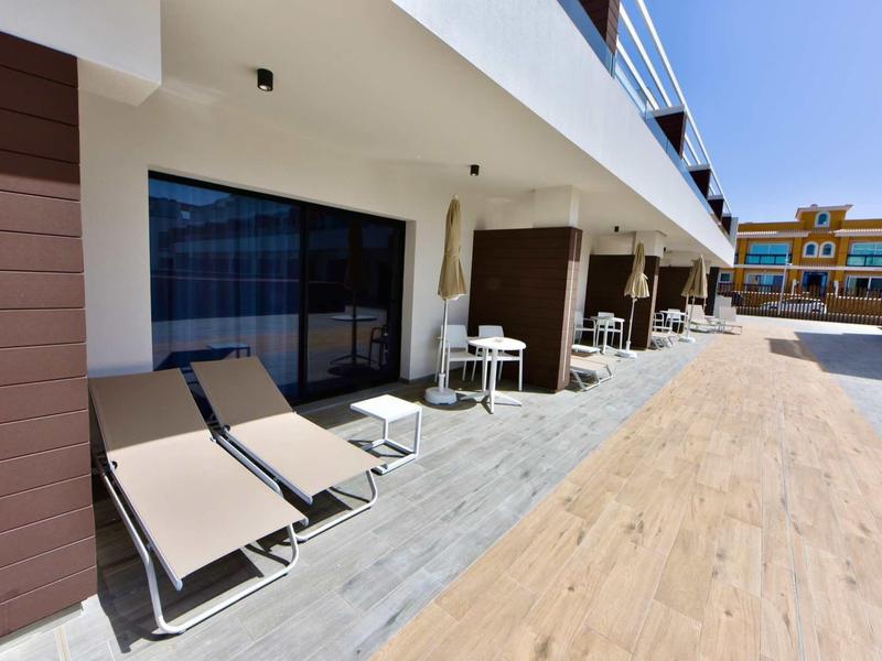 Terrasse d'hôtel ensoleillée avec chaises longues et tables devant les portes des chambres par jour dégagé.