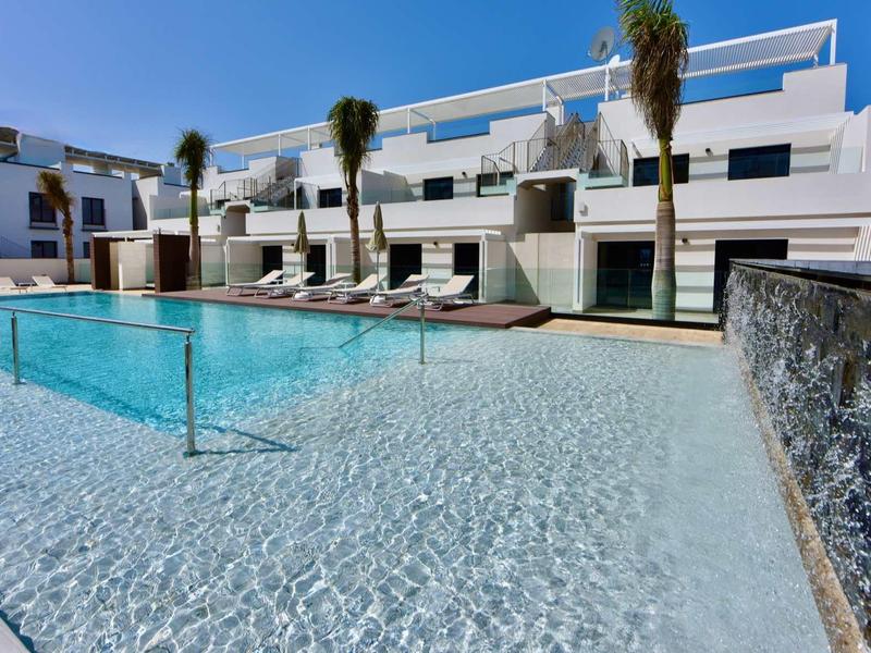 Piscine d'hôtel moderne avec eau bleu clair, transats et bâtiments blancs par temps ensoleillé.