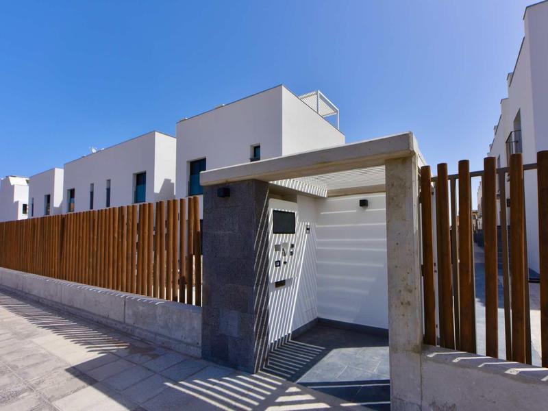 Entrée de maison moderne avec façade blanche, clôture en bois et ciel clair en arrière-plan.