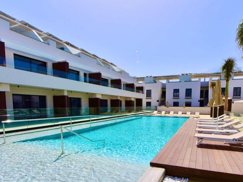 Piscine d'hôtel moderne avec chaises longues et palmiers sous un ciel dégagé.