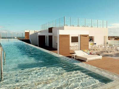 Piscina infinita en la azotea con tumbonas y terraza moderna del hotel bajo cielo despejado.