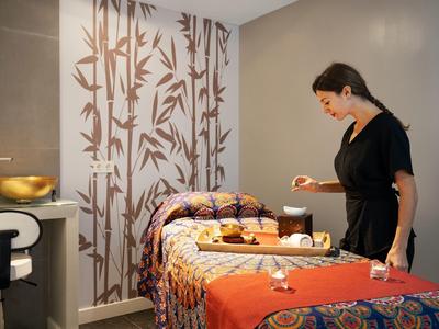 Una mujer prepara una camilla de masaje en una acogedora habitación de spa con colores cálidos.