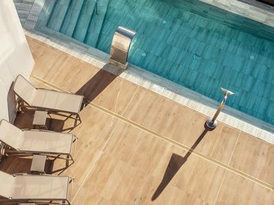 Quatre chaises longues à côté d'une piscine avec une terrasse en bois et une poubelle à l'ombre.