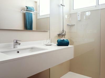 Baño moderno y luminoso con lavabo blanco, toallas y área de ducha con pared de vidrio.