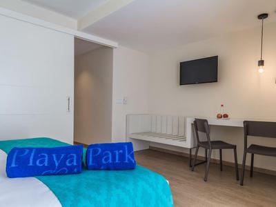 Helles Hotelzimmer mit zwei Betten, Fernseher und Schreibtisch mit zwei Stühlen.