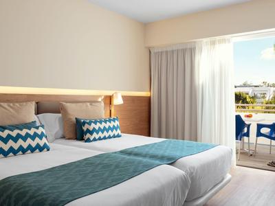 Modernes Hotelzimmer mit zwei Einzelbetten, blau-weißem Bettzeug und Balkon mit Blick ins Grüne.