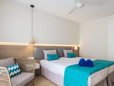 Habitat luminoso con cama doble, toques turquesas y sillón cómodo.