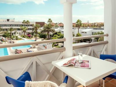 Balkontisch mit zwei blauen Stühlen, Blick auf Pool und Hotelanlage bei klarem Himmel.
