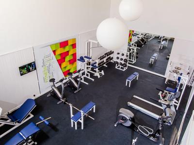 Salle de sport moderne avec appareils de musculation, haltères et grands miroirs aux murs.