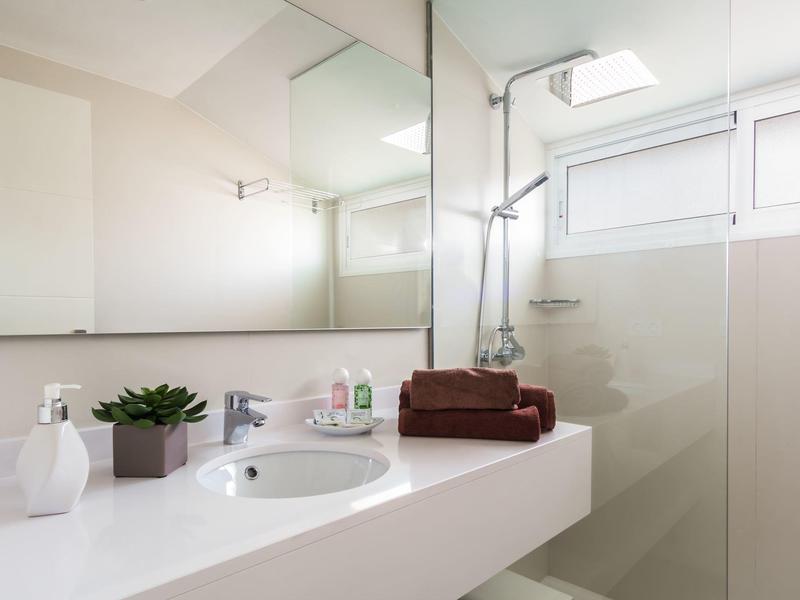 Baño luminoso con lavabo, espejo, área de ducha y planta decorativa en estilo moderno.