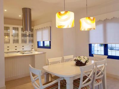 Bright kitchen with round dining table, white chairs, and two hanging lamps.