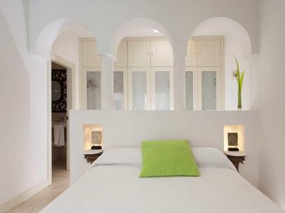 Dormitorio con cama blanca, cojín verde y arcos decorativos en una habitación luminosa.