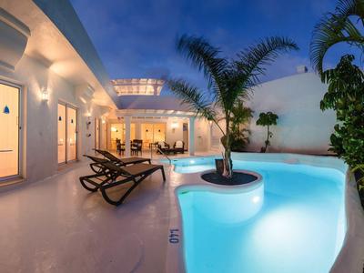 Modern outdoor pool area at night with loungers and tropical plants.