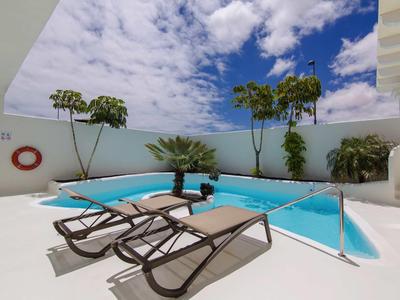 Modern pool area with sun loungers and tropical plants under a blue sky.