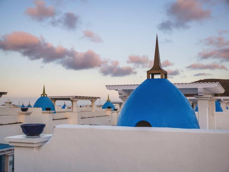 View of white buildings with blue domes and bell towers at sunset.