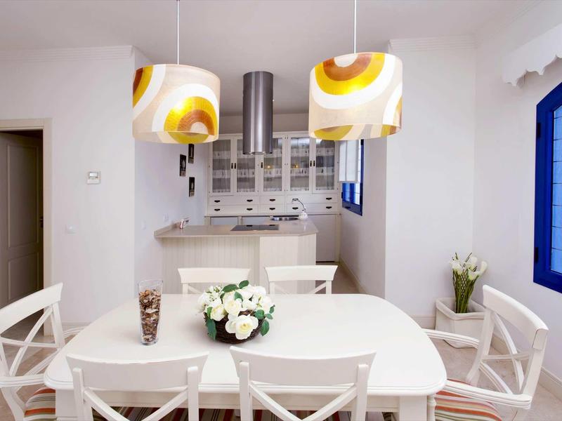 Modern dining area with white table and chairs, flowers, and kitchen in the background