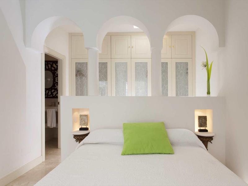 Simple white bedroom with green pillow and decorative arches on the wall