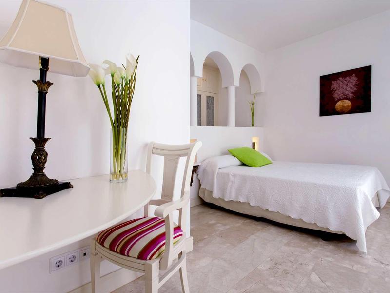 White furnished bedroom with simple bed, chair, and black lamp