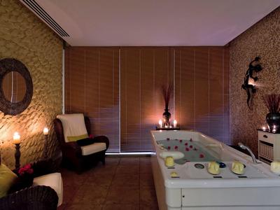 Cozy spa room with jacuzzi, soft lighting, armchairs, and decorative candles and flowers.