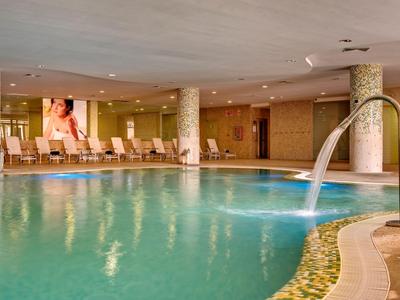 Innenpoolbereich mit Liegestühlen, Wasserfall und entspannter Atmosphäre in einem Hotel