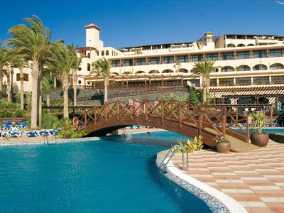 Ein Hotel mit einem Brückenweg über einen blauen Pool und Palmen am Rand.