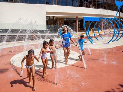 Children playing and running through outdoor water fountains on a sunny day.