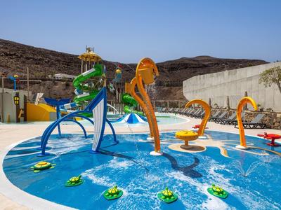 Outdoor water playground with colorful animal-shaped fountains and slides in a hotel pool area.