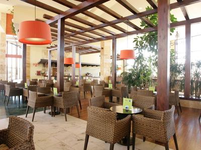 Geräumiges Restaurant mit Korbsesseln, Holzbalken und großen Fenstern für viel Tageslicht.