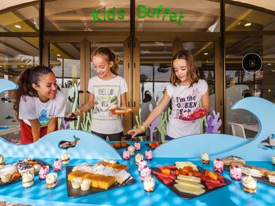 Three girls enjoying snacks and treats at a table with blue wave decorations in a hotel lobby.