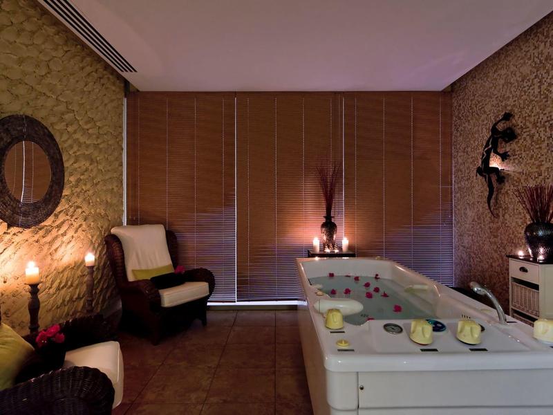 Cozy spa room with jacuzzi, soft lighting, armchairs, and decorative candles and flowers.