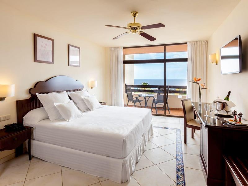 Spacious hotel room with double bed, balcony, ocean view, and modern furnishings.