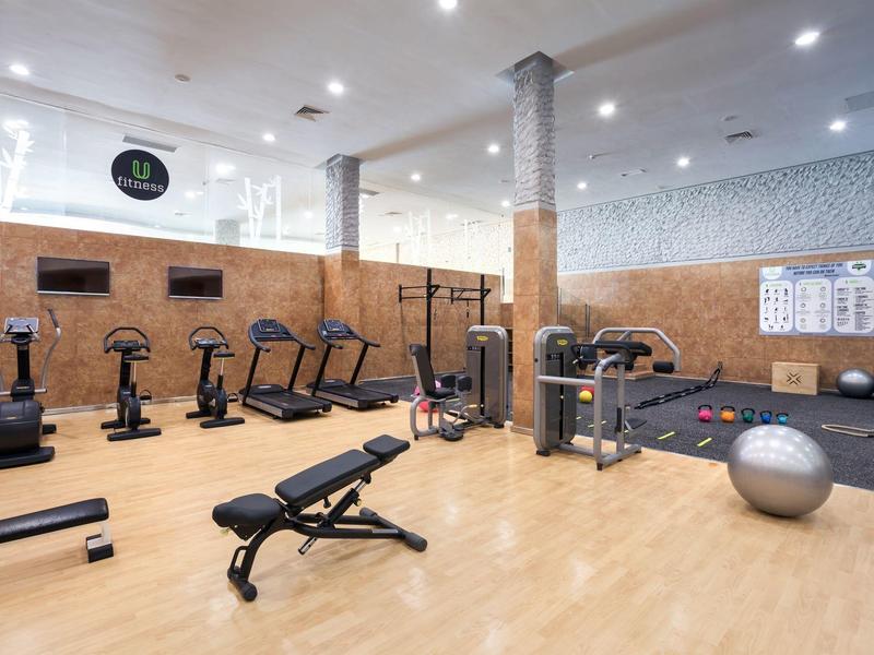 Spacious gym with cardio machines, weight bench, exercise balls, and modern equipment on wood floor.