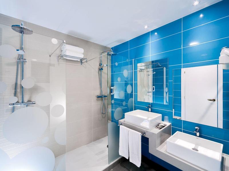 Modern bathroom with blue tiled wall, double sinks, and walk-in shower with glass door.