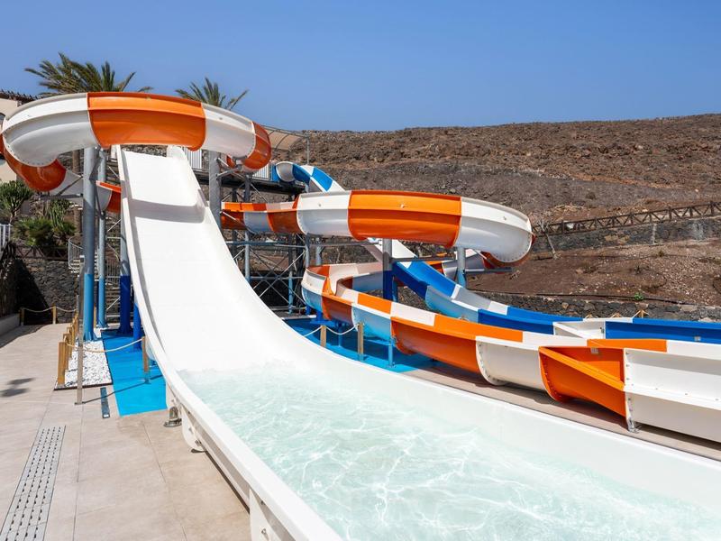 Large water slides with orange and white stripes in a sunny water park at a resort.