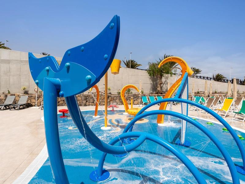 Colorful water playground with slides and splash features near hotel loungers on a sunny day.