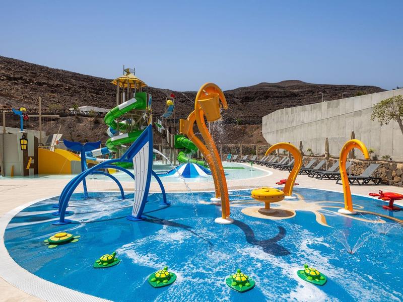Outdoor water playground with colorful animal-shaped fountains and slides in a hotel pool area.