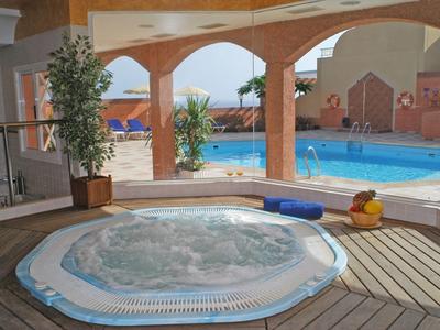 Bañera de hidromasaje interior con vista a una piscina y plantas en un hotel.