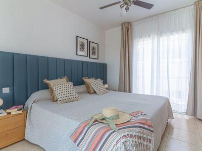 Hell eingerichtetes Schlafzimmer mit großem Bett, blauem Kopfteil und beigen Vorhängen.