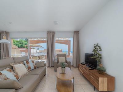 Helles Wohnzimmer mit grauem Sofa, Holzsideboard, großem Fenster und Blick auf Terrasse und Garten.