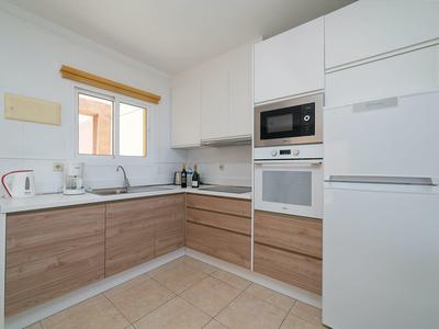 Moderne Küche mit weißen Wänden, Holzschränken, weißem Kühlschrank und eingebauten Geräten.