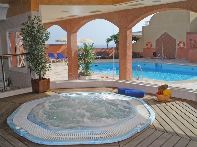 Bain à remous dans une zone couverte avec vue sur une piscine extérieure et des chaises longues.