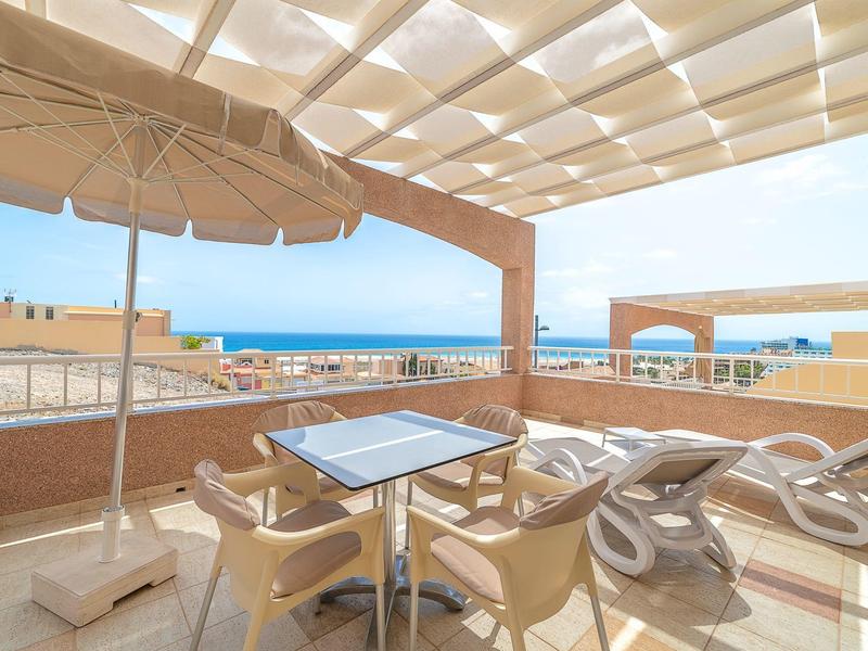 Terrasse avec sièges et transats avec vue sur la mer sous une couverture d'ombrage.