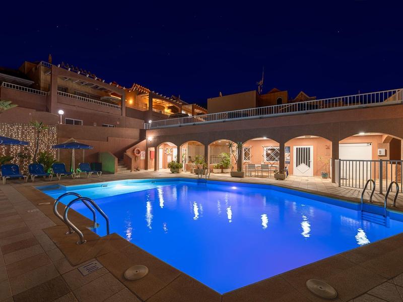 Piscine d'hôtel éclairée avec chaises longues et terrasse sur le toit la nuit
