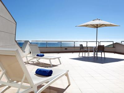 Taras na dachu z leżakami, parasolem i miejscami do siedzenia z widokiem na morze.