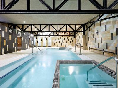 Piscina interior moderna con dos piscinas, chimeneas y vigas en el techo.